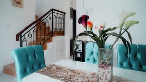 A dining area with teal upholstered chairs, a glass table, and a vase with flowers. - Been View Homestay (Berbah)