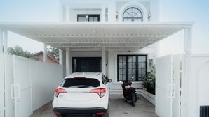 A white two-story house with a covered driveway, a white car, and a red motorcycle parked outside. - Been View Homestay (Berbah)
