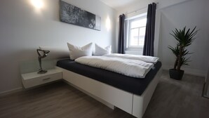A modern bedroom with a bed, bedside table, lamp, and a potted plant. - Vacation apartment "Rhön" (Bad Salzungen)