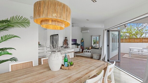 Una cocina moderna con armarios blancos, un gran comedor de madera y una lámpara colgante.