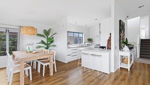 Una cocina moderna con armarios blancos, una isla central con taburetes de bar y un comedor con mesa y sillas de madera.