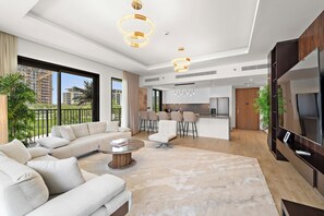 Sala moderna com sofá, mesa de centro e televisão. Há uma cozinha com balcão e mesa de jantar. O espaço possui grandes janelas e uma varanda.