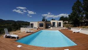 A modern pool area with a rectangular pool, wooden deck, and white lounge chairs. - Spacious Villa in Vagnas with Pool (Vagnas)