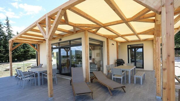 A covered outdoor area with a wooden structure, tables, chairs, and lounge chairs. - Spacious Villa in Vagnas with Pool (Vagnas)