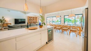 A modern kitchen with a large island, dining area with wicker chairs, and a TV in the living room. - Conch Beach Villa NEW 7-Bed 6 Bath Pool 5-min to Beach by Bocobay (Noord)