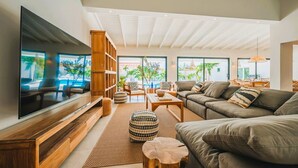 A spacious living room with a large flat-screen TV, comfortable seating, and a view of the outdoors. - Conch Beach Villa NEW 7-Bed 6 Bath Pool 5-min to Beach by Bocobay (Noord)