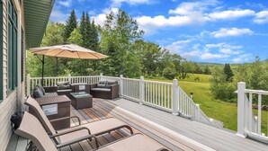 Una terraza con mobiliario exterior, barandilla blanca y vistas a un paisaje verde.