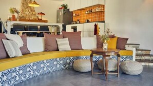 Una sala moderna con un sofá estampado en amarillo y azul, una pequeña mesa de madera y una zona de cocina con pared de piedra y azulejos naranjas.