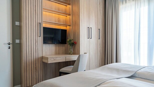Une chambre d’hôtel moderne équipée d’un bureau en bois, d’un téléviseur à écran plat, d’une chaise et d’un lit.