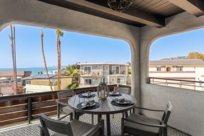 A balcony with a round table set for dining, overlooking a coastal area with palm trees and buildings. - 3 Condos, Steps to Beach, Rooftop Patio | Trestles Trailhead Trio by AvantStay (San Clemente)