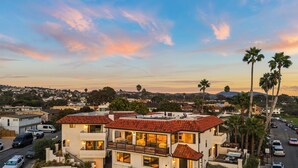 Une maison moderne à deux étages, avec un toit recouvert de tuiles rouges, un balcon et une vue sur le quartier environnant.