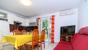 A compact living space with a dining area, a red sofa, a TV, and a sliding glass door leading to a garden. - Beachfront apartment fully equipped with outdoor garden space, parking included. (Okrug Gornji)