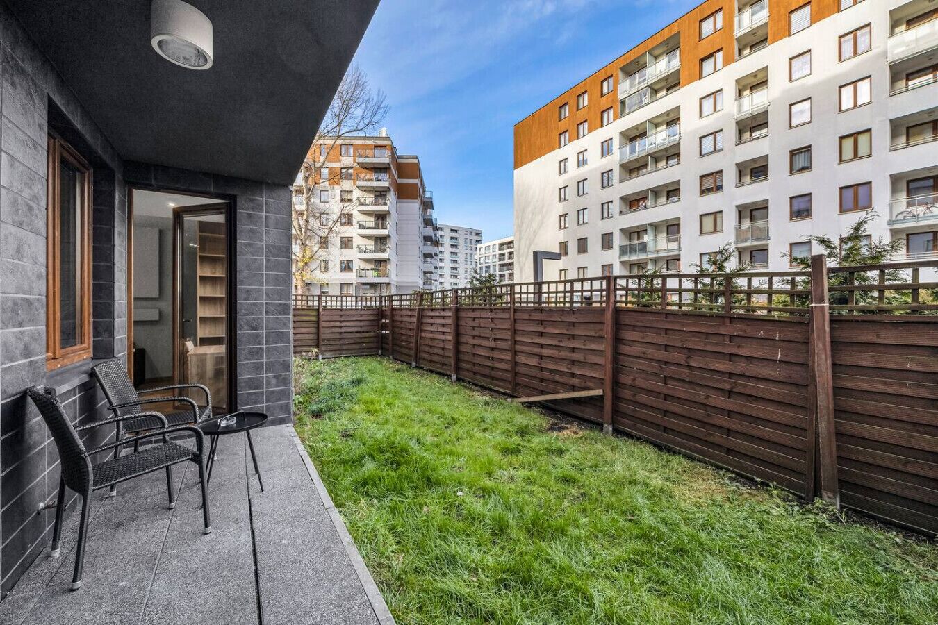A modern apartment with a balcony, a wooden fence, and a view of neighboring buildings.