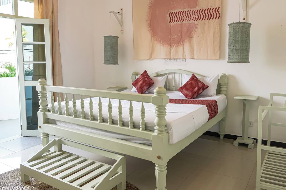 A bed with a white headboard and footboard, a bedside table, and a wall-mounted lamp.