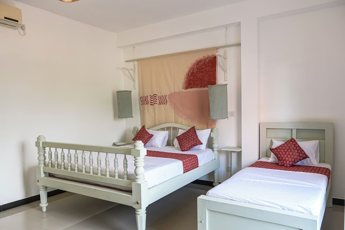 A room with two beds, a hanging light fixture, a wall-mounted air conditioner, and a woven rug.