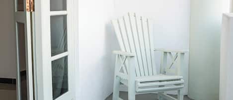 Une chaise blanche est placée contre un mur blanc, à côté d’une porte blanche dotée de panneaux de verre.