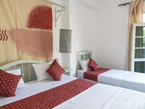 A hotel room with two beds, each with white linens and red patterned bedspreads. There is a large window with curtains, a wall-mounted lamp, and a wall sconce. - Mira Mirissa  (Mirissa)