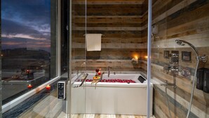 A modern bathroom with a large bathtub, a glass shower enclosure, and a view of the sunset through a large window. - Moustache Select Mcleodganj (Dharamshala)