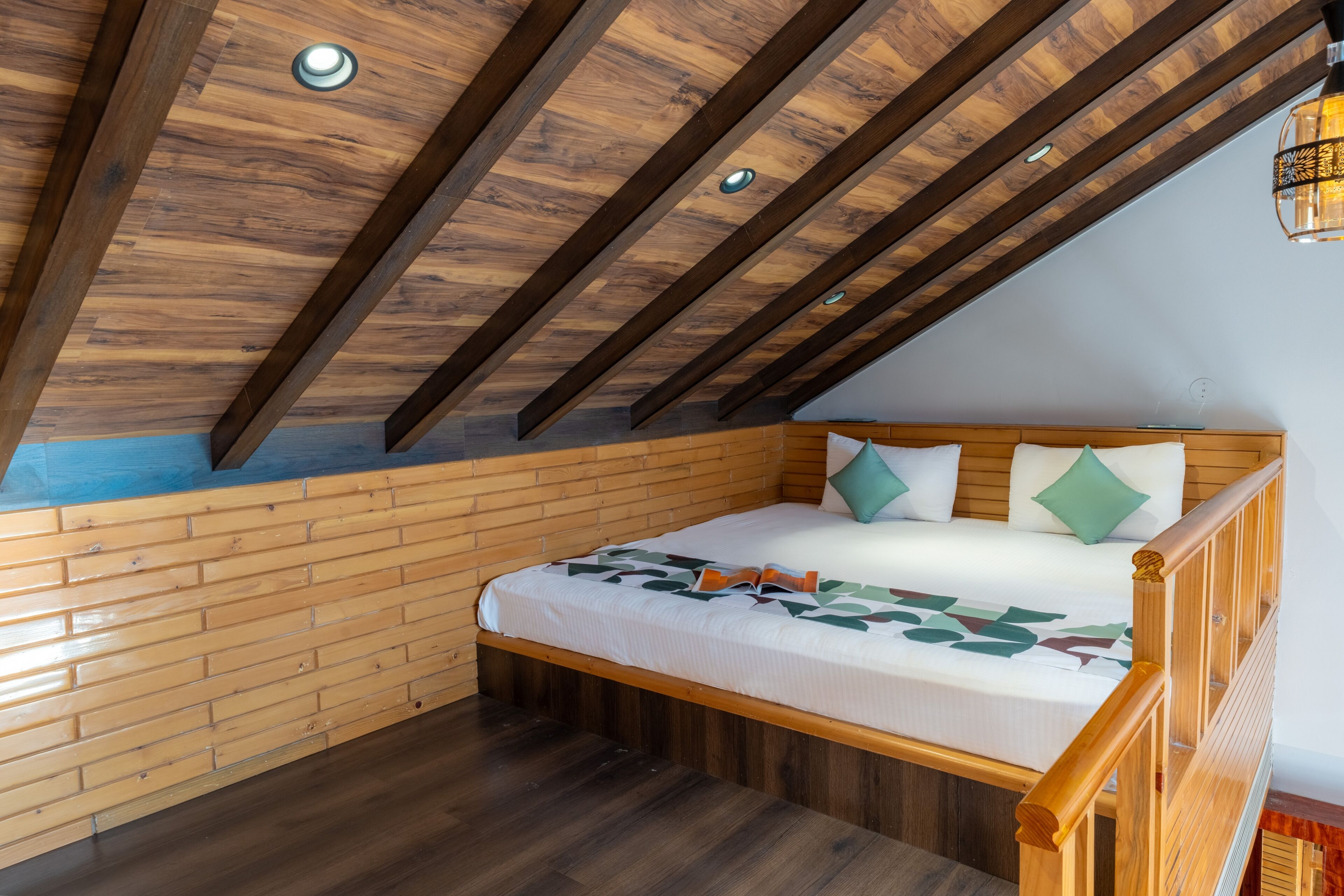 Een slaapkamer met een schuine plafond, houten balken, een bed met kussens en een houten vloer.