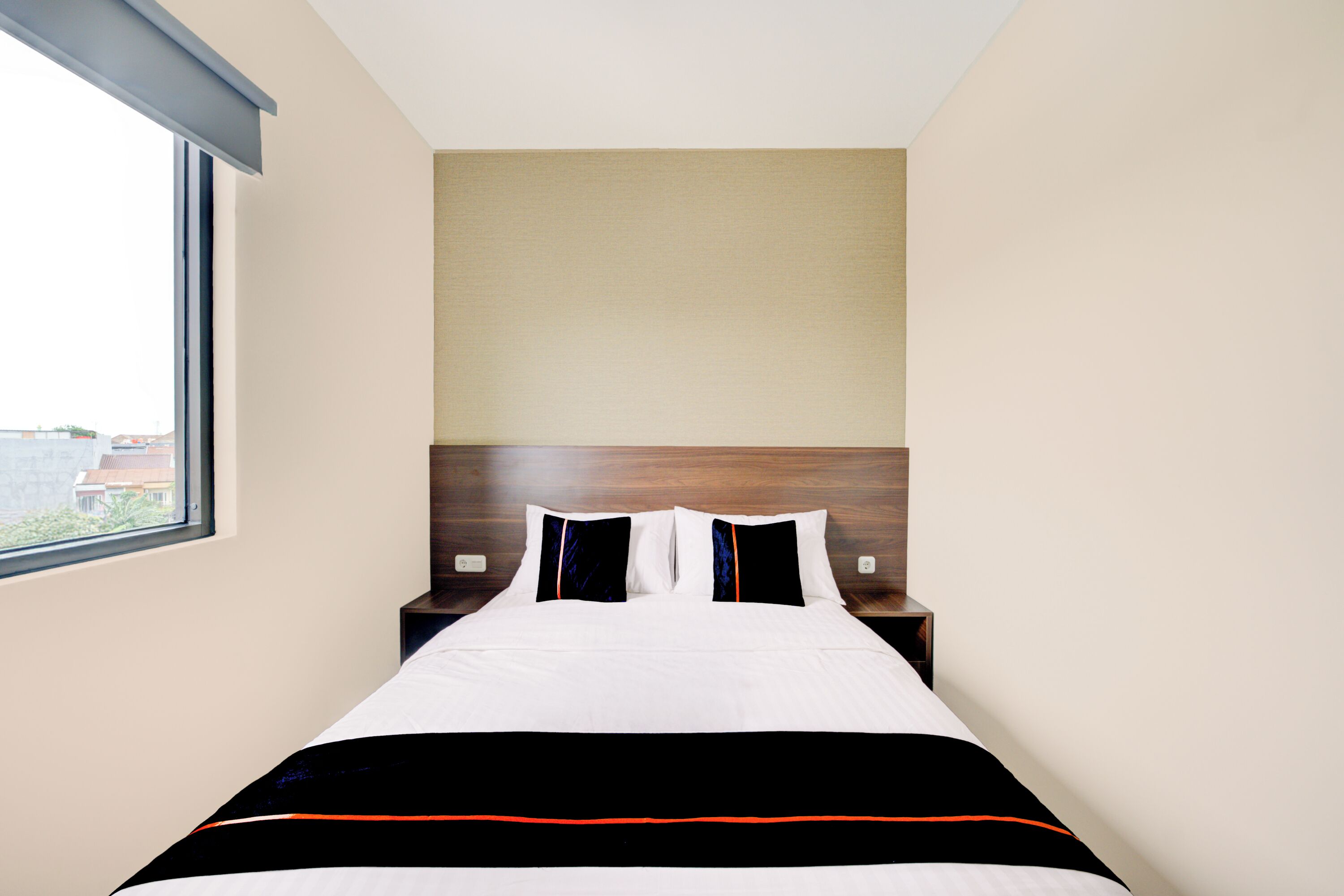 A hotel room with a large bed, a wooden headboard, and a window providing a view of the outside.