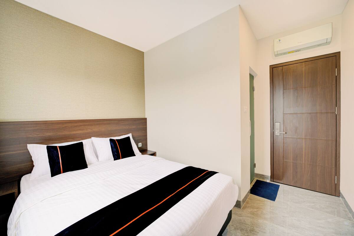 A hotel room with a large bed, a wooden headboard, a door, and an air conditioning unit on the wall.