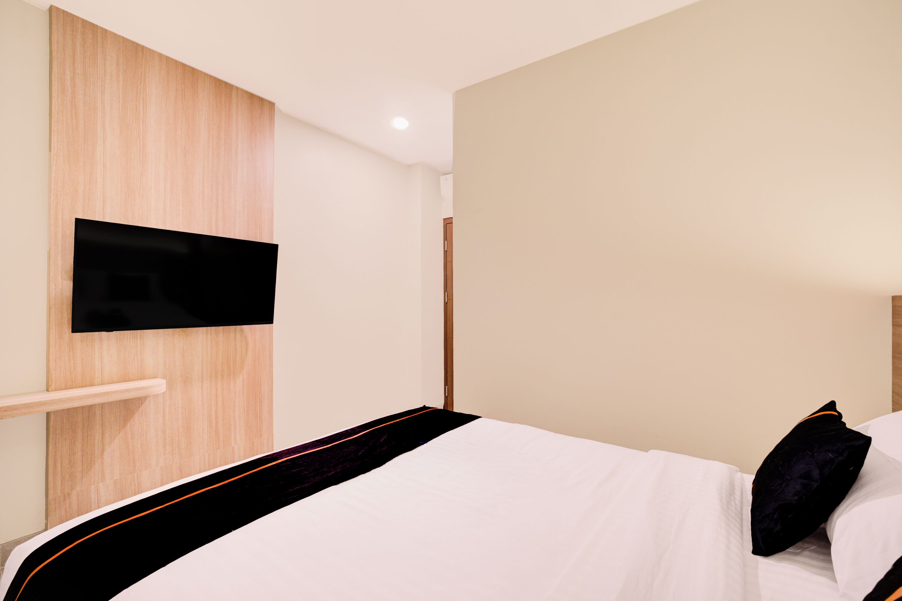 A hotel room with a bed, a mounted TV, and a wooden panel wall.
