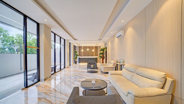 Een moderne woonkamer met een bank, fauteuils en een salontafel. Er is een open haard en een groot raam met uitzicht op de omgeving.