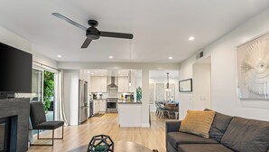A modern living room with a sofa, a coffee table, and a TV. There is a kitchen in the background with a dining area. - 2 Condos | Steps to the Beach + Hot Tub | Trestles Trailhead Duo by AvantStay (San Clemente)