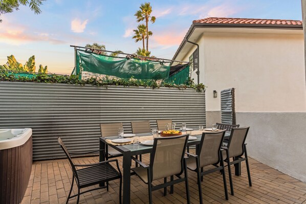 An outdoor dining area with a table set for six, surrounded by chairs, a hot tub, and a green canopy.