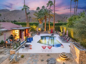 Un jardin avec une piscine, des chaises longues et un espace barbecue.