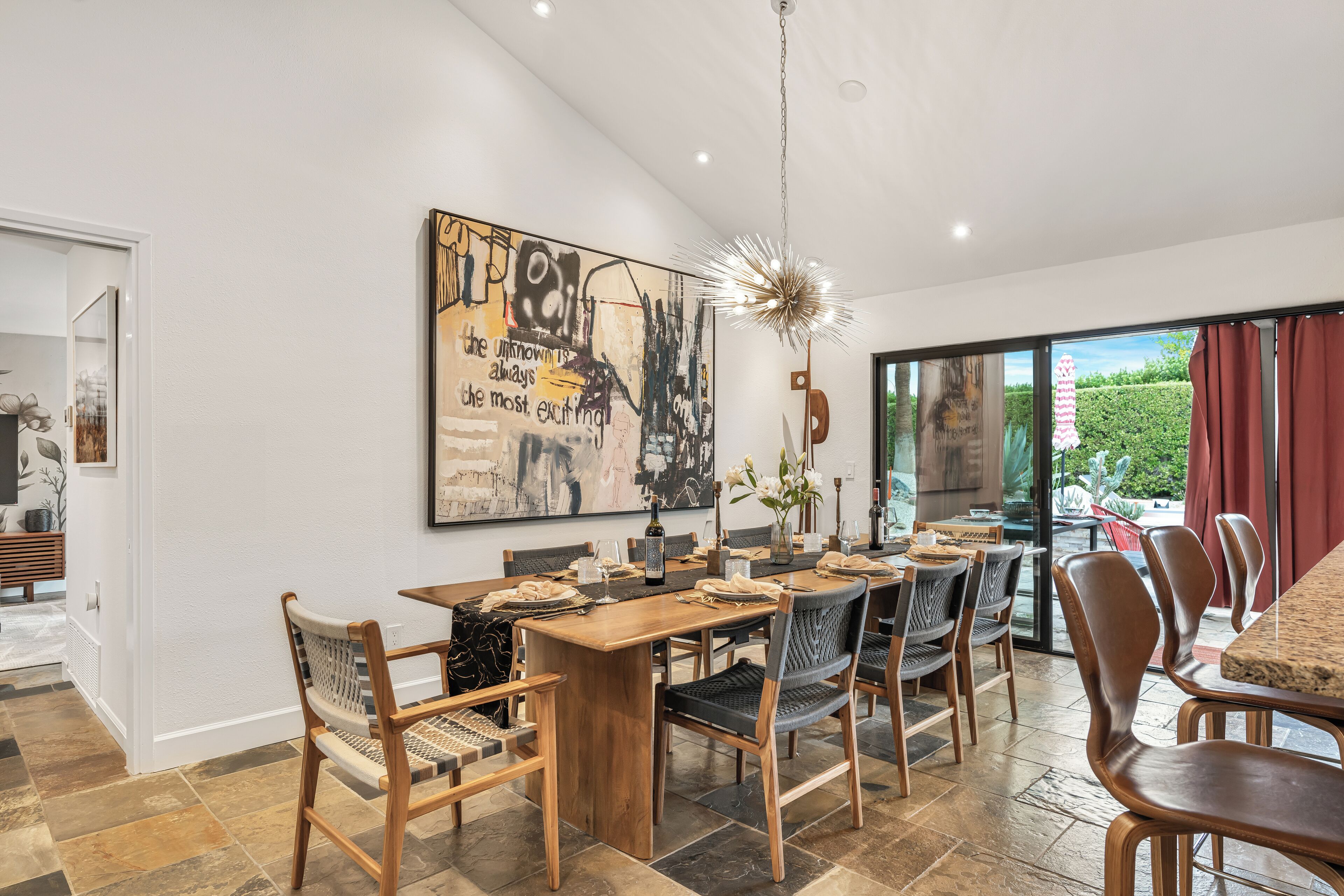 A modern dining area with a wooden table and chairs, a large abstract painting, and a view through a glass door.