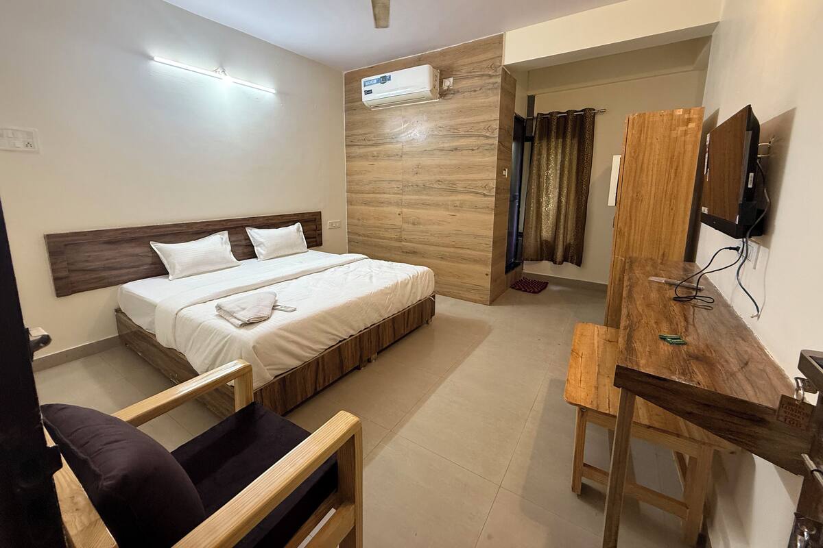 A hotel room with a bed, a desk, a chair, a ceiling fan, an air conditioning unit, and a television.