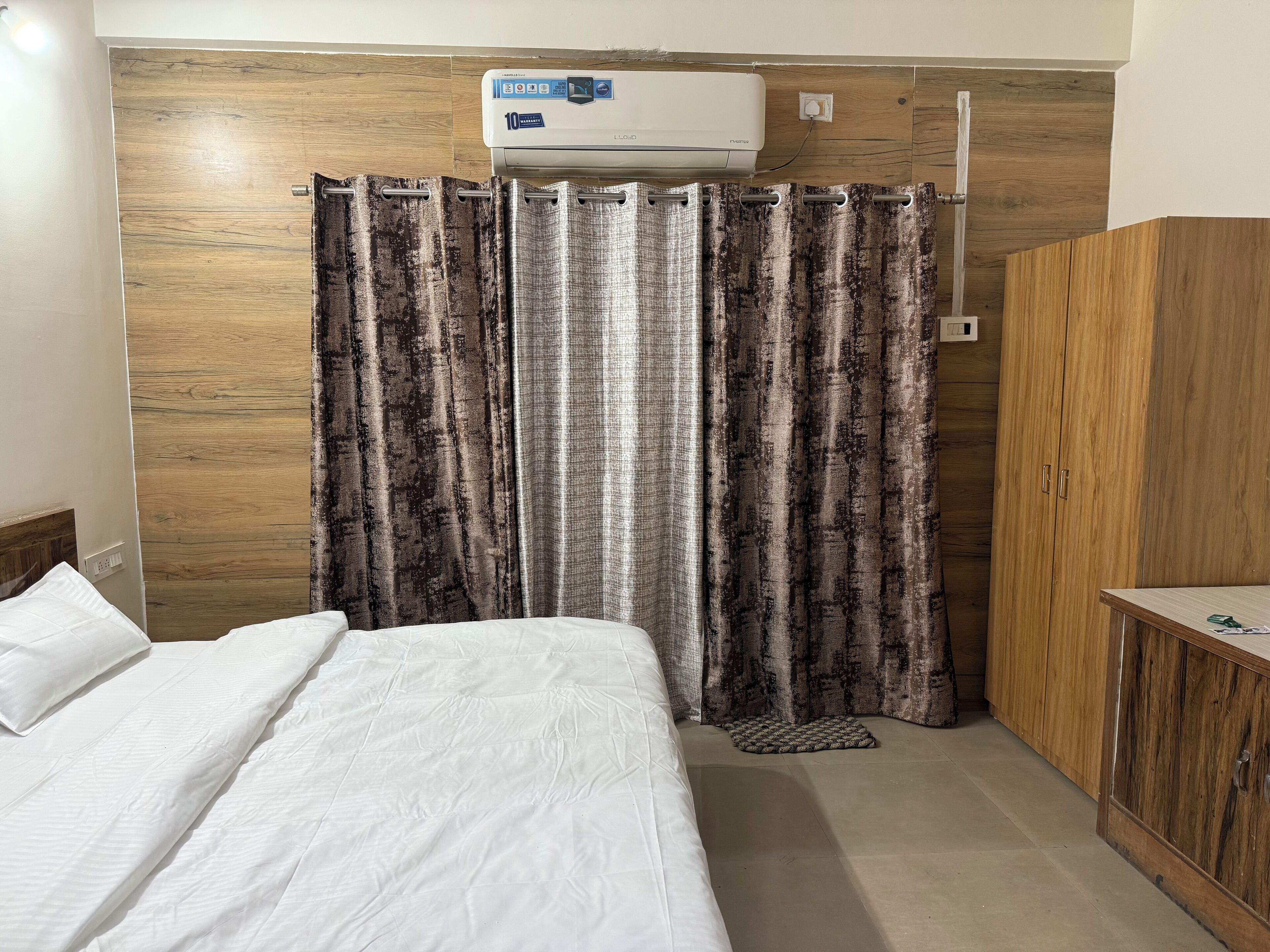 A bedroom with a bed, a wooden wardrobe, a curtain, and an air conditioning unit.