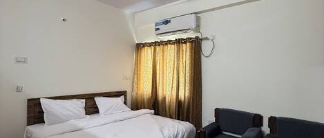 A bedroom with a bed, a ceiling fan, an air conditioning unit, a sofa, and a wooden table.