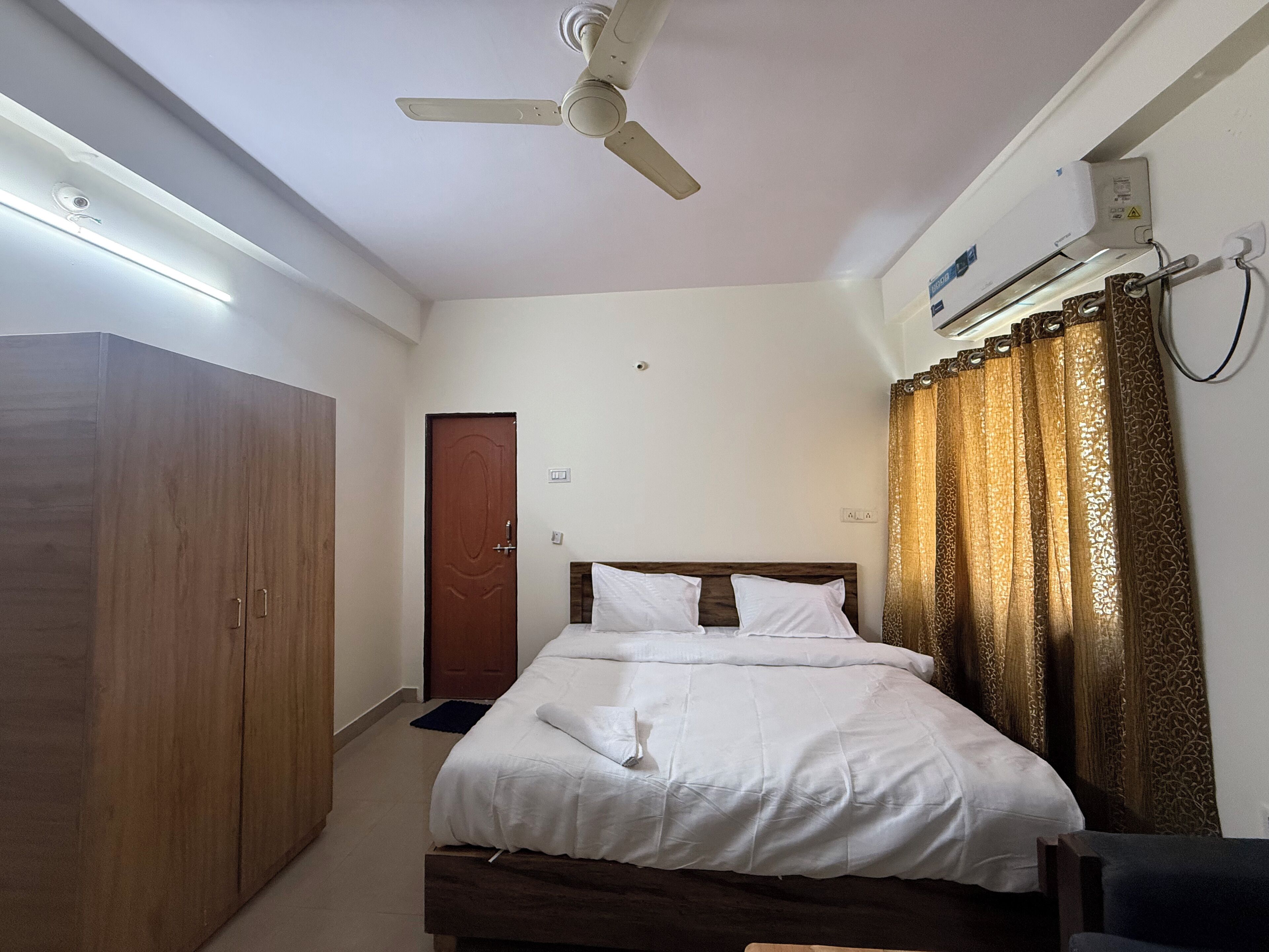 A bedroom with a bed, wardrobe, ceiling fan, air conditioning unit, and a door.