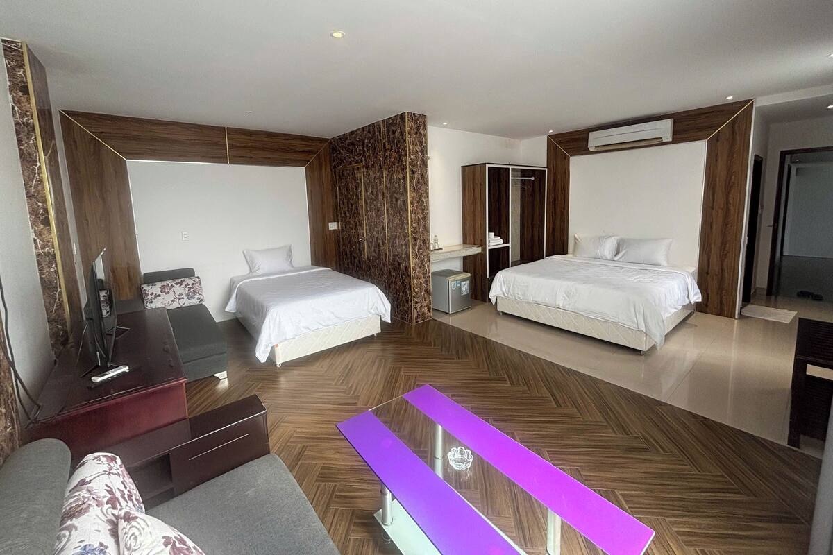 A modern hotel room with two beds, a desk, and a seating area.