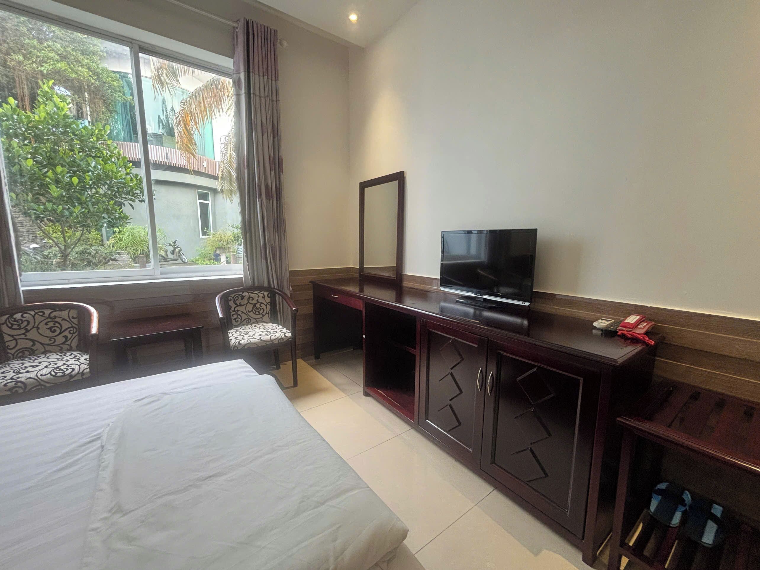 A hotel room with a bed, a desk with a TV, a chair, and a window with curtains.