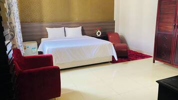 Una habitación de hotel con una cama, un sillón rojo, un armario de madera y una mesita de noche con un jarrón de flores.