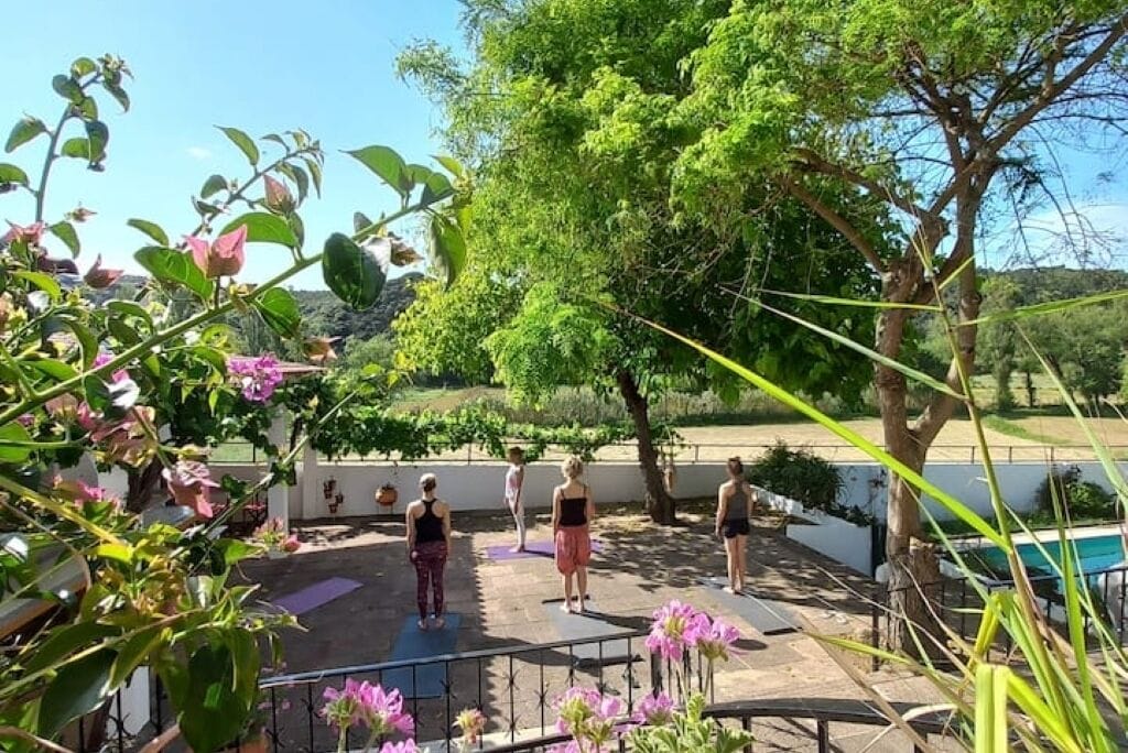 A group of people exercising outdoors with trees and a pool in the background.