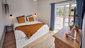 Ein Schlafzimmer mit einem Bett, Nachttischen, einer hölzernen Kommode und Blick durch eine Glastür.
