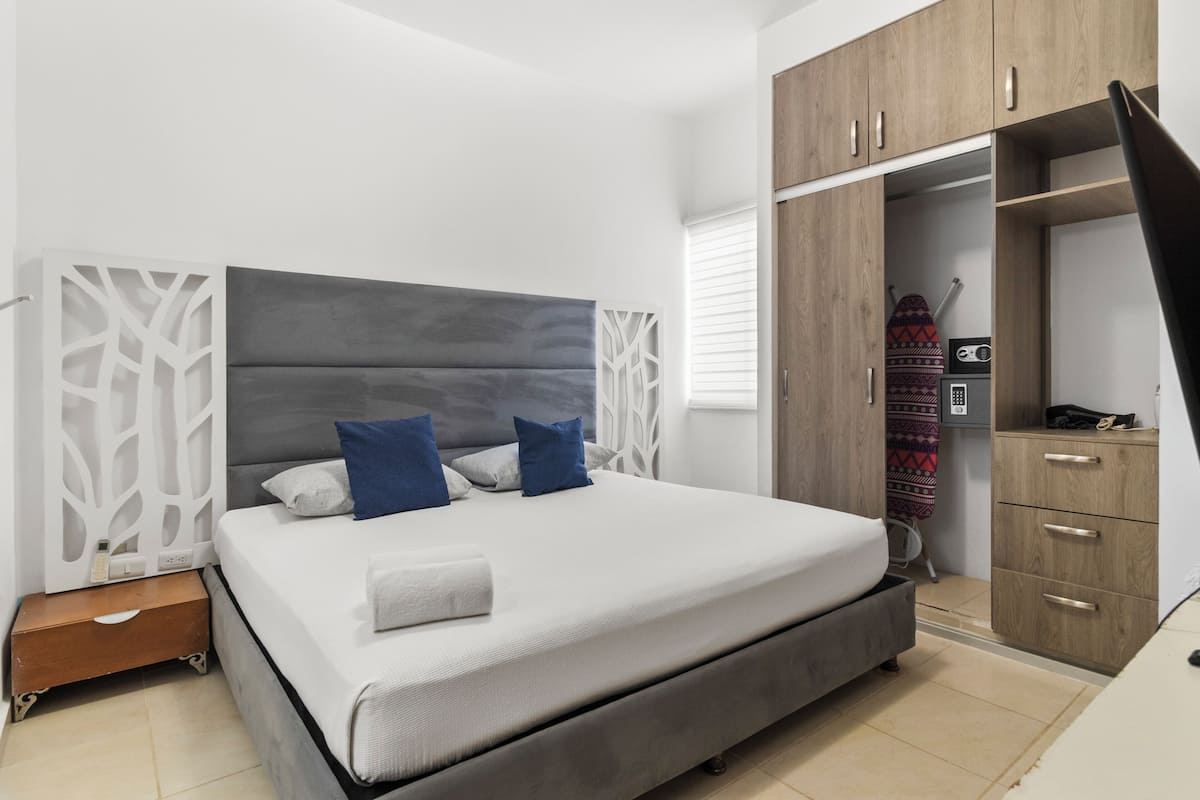A modern bedroom with a large bed, a wardrobe, and a small bedside table.