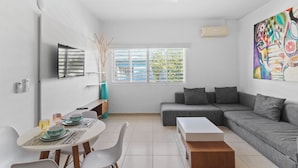 Una sala de estar moderna con un sofá gris, una mesa de centro blanca y una zona de comedor con una mesa y sillas blancas.
