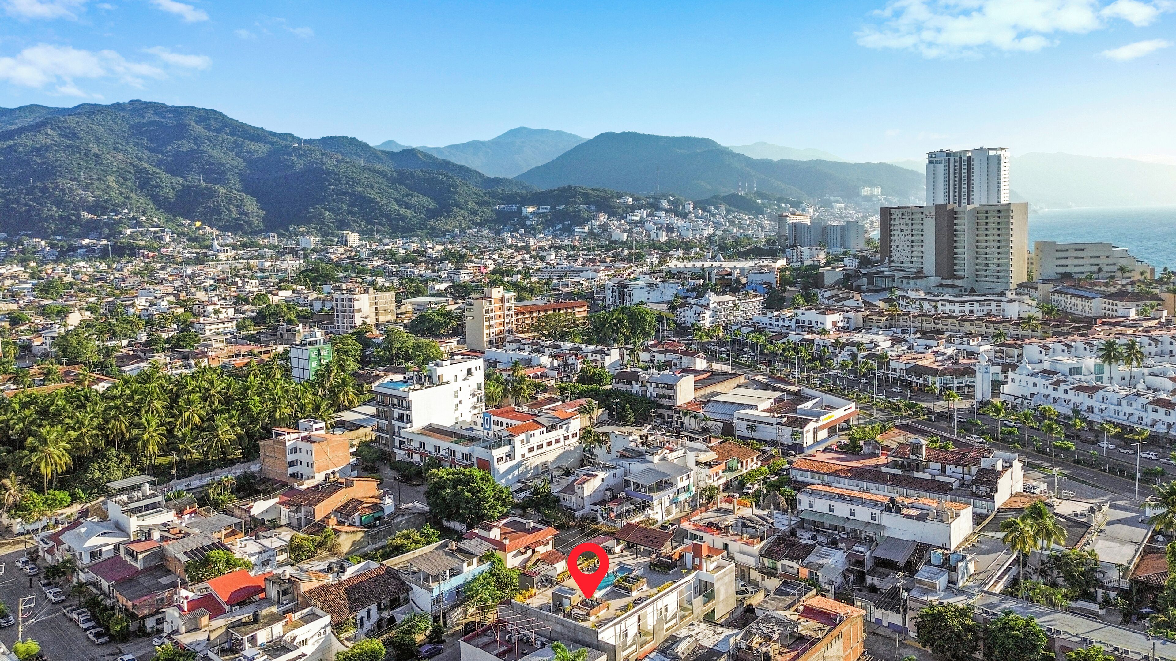 Un paisaje urbano con edificios residenciales densos, un llamativo hito rojo, y montañas con un cielo despejado al fondo.
