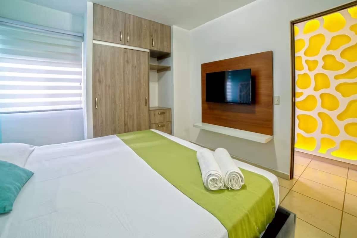 A hotel room with a bed, a TV mounted on the wall, and a wardrobe.