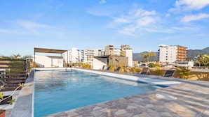Piscina con baldosas de piedra, rodeada de sillones de descanso y una pérgola.