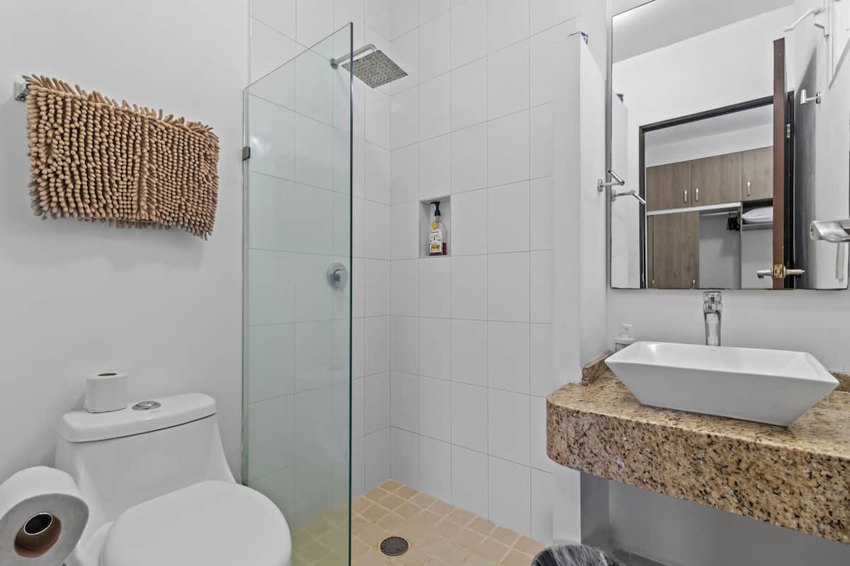 A modern bathroom with a glass-enclosed shower, a toilet, a sink with a granite countertop, and a wooden towel rack.