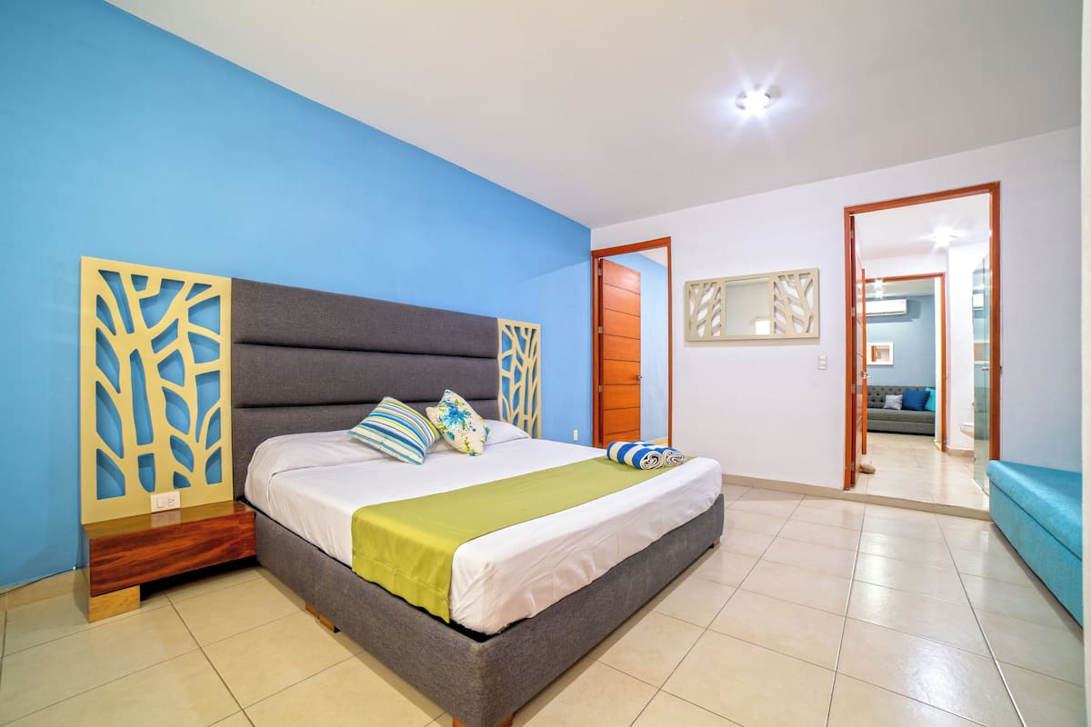 A bedroom with a bed, a wooden nightstand, a blue wall, a grey headboard, and a wooden door.