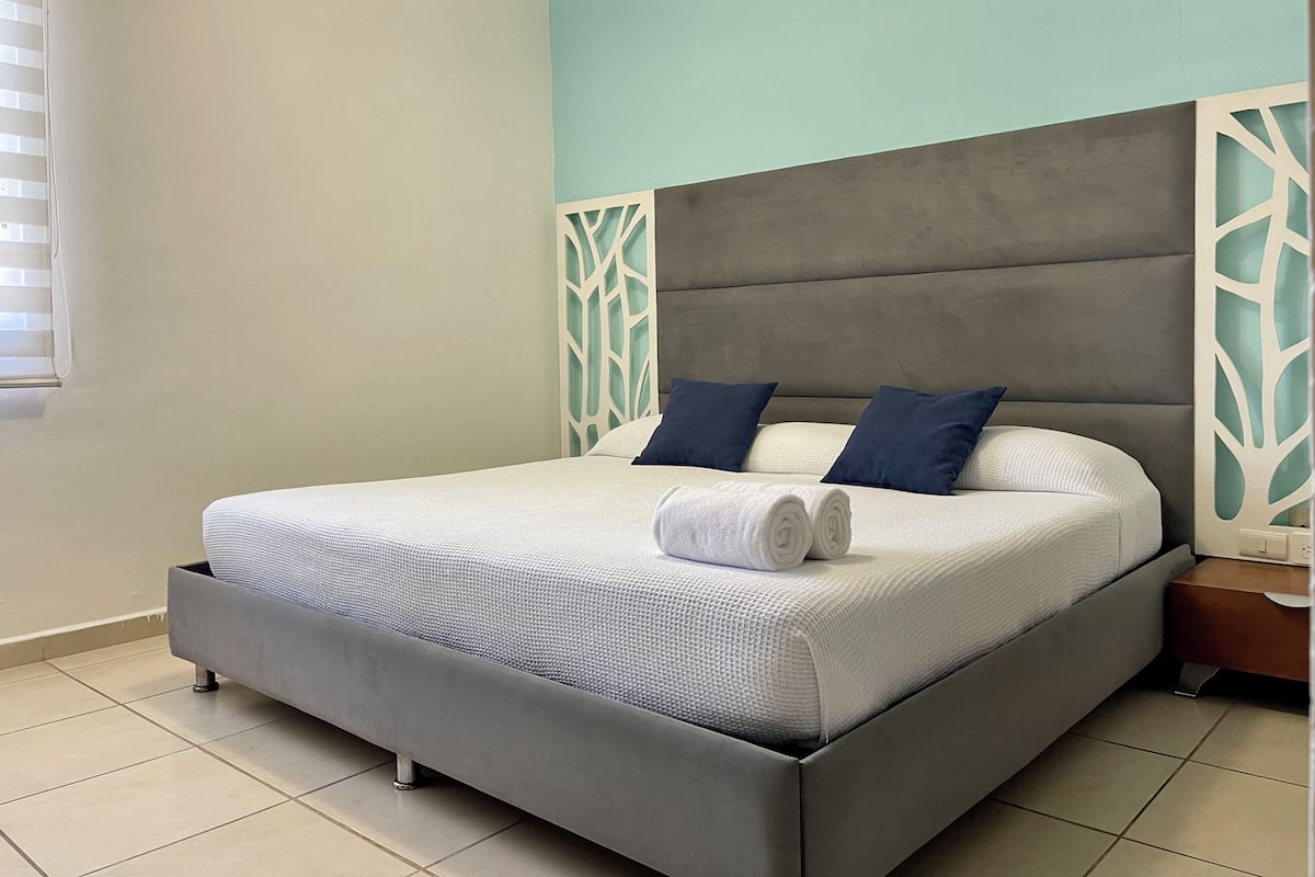 A modern bedroom with a grey bed, white linens, and blue pillows.