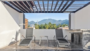 Un espacio de estar al aire libre cubierto con dos sillas y una mesita, con vistas a una cordillera y palmeras.