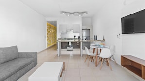 Una sala de estar moderna con un sofá gris, una mesita de centro blanca y una zona de comedor con sillas blancas y una pequeña mesa.